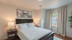 A bedroom with a bed, two bedside tables, a nightstand, a headboard, and a window with curtains. - Murfreesboro Gem Near Square + MTSU - Cozy Cottage (Murfreesboro)