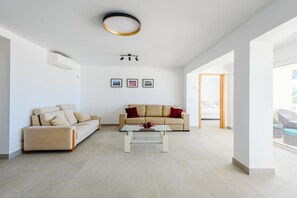 Ein geräumiges Wohnzimmer mit einem beigefarbenen Sofa, einem Glastisch und einer modernen Deckenleuchte.