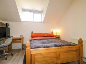 Ein Schlafzimmer mit schrägen Wänden, einem Bett mit orangefarbener Bettwäsche, einem Schreibtisch mit Stuhl, einer Lampe und einer Heizung.