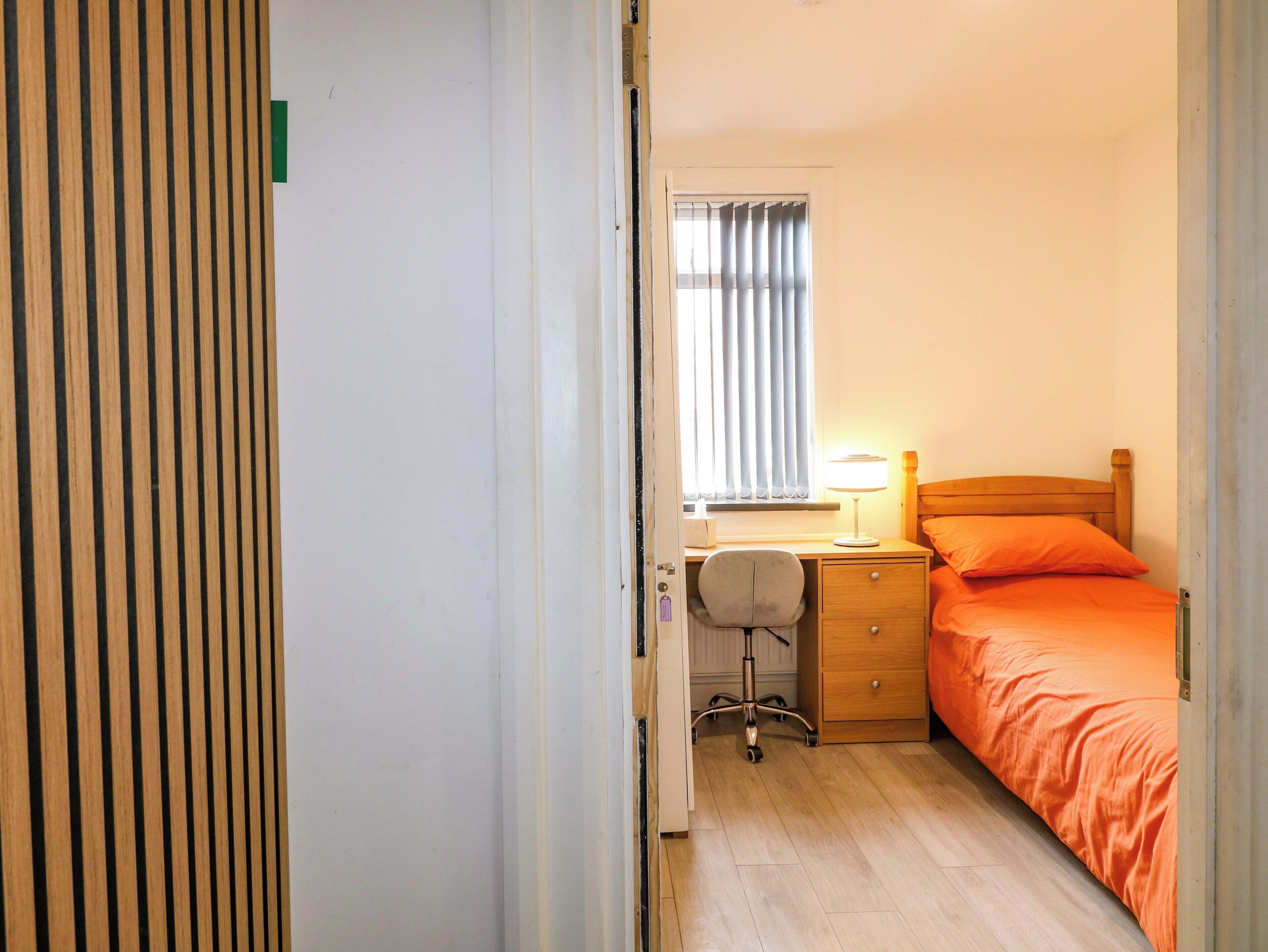 A bedroom with a bed, desk, chair, and a window with curtains.