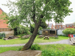 Ein Garten mit Picknicktischen, einer Pergola und einer Ziegelmauer.