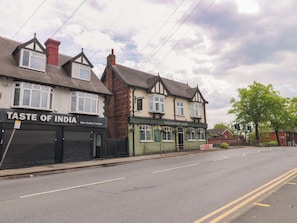 Eine Straße mit Gebäuden, darunter ein Restaurant namens 'The Johnson Arms' und ein Geschäft mit dem Namen 'Taste of India'.