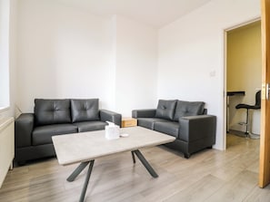 Ein modernes Wohnzimmer mit zwei dunkelbraunen Ledersofas, einem hellen Couchtisch und Holzböden.