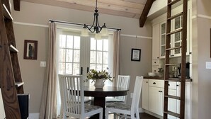 Un comedor con una mesa redonda, sillas blancas, una araña y una cocina con armarios de madera y una escalera.