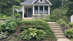 Una casa pequeña con porche, escalones que llevan a la entrada y un jardín con diversas plantas.