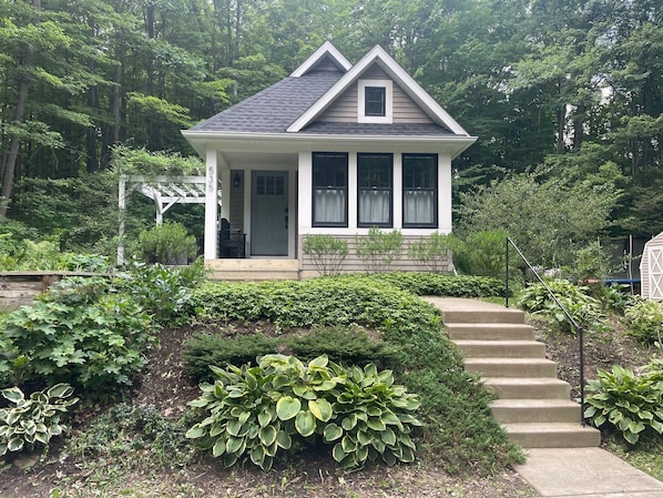 A small house with a porch, steps leading to the entrance, and a garden with various plants.