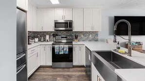 Una cocina moderna con armarios blancos, electrodomésticos de acero inoxidable, salpicadero de azulejos y un ventanal grande.