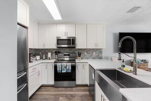 A modern kitchen with white cabinets, stainless steel appliances, a tiled backsplash, and a large window. - Panama Beach Getaway (Panama City Beach)