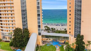 Un hotel moderno de gran altura con varios balcones, una zona de piscina con fuentes de agua azules y vistas al océano.