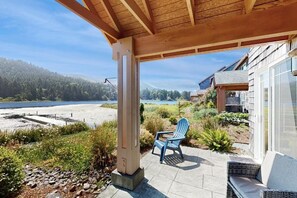 En overdækket terrasse med udsigt over sø og skov, en blå Adirondack-stol og en stikvej af sten.