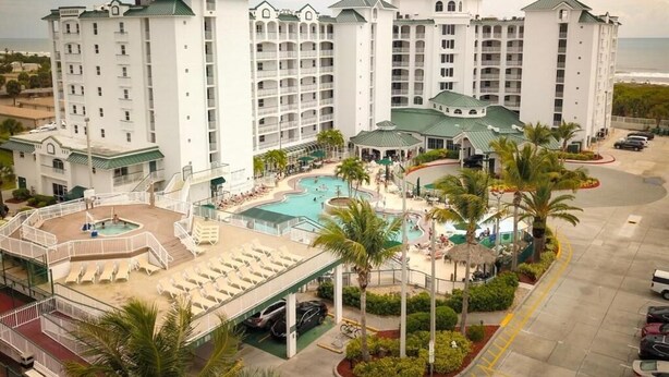 A multi-story hotel with a pool area, palm trees, and a view of the ocean. - Cozy 2-bedroom apartment in charming Cocoa Beach with AC (Cocoa Beach)