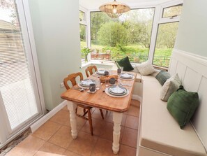 A conservatory with a dining table set for four, surrounded by chairs, and a bench with cushions. - The Lodge (Alnwick)