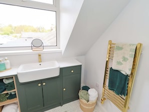 A bathroom with a window, a sink, a mirror, a towel rack, and a basket with towels. - The Lodge (Alnwick)