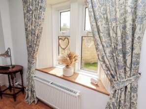 A room with a window, a radiator, a desk with a lamp, and a vase with dried plants. - The Lodge (Alnwick)