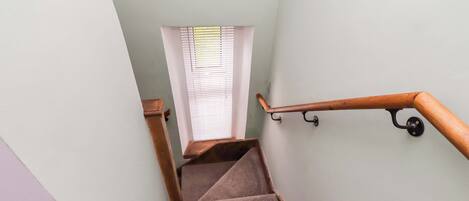 A staircase with carpeted steps, wooden handrails, and a window with blinds.