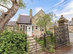 A stone house with a white door, a chimney, and a gated entrance. - The Lodge (Alnwick)