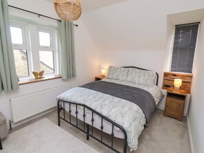 A bedroom with a bed, a bedside table with a lamp, a window with curtains, and a radiator. - The Lodge (Alnwick)
