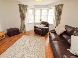 A living room with a brown leather sofa, a brown leather armchair, a matching ottoman, a patterned rug, and a window with curtains. - The Lodge (Alnwick)