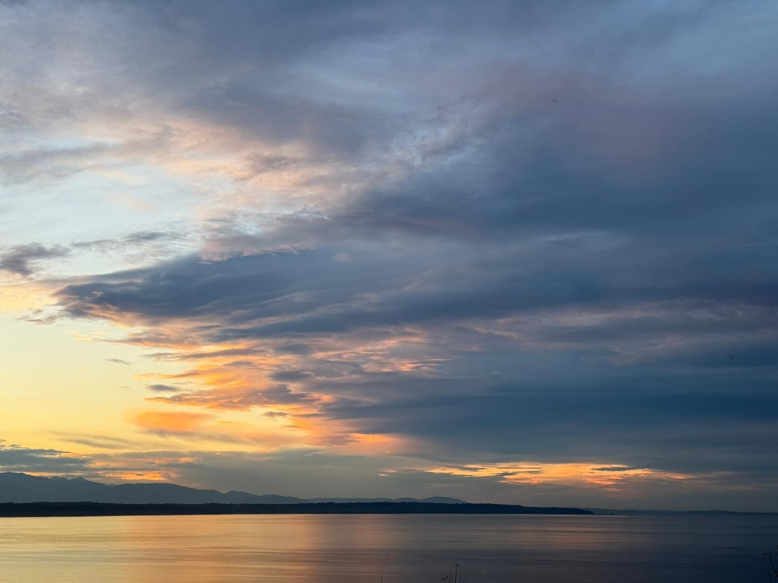 A calm body of water with a distant mountain range and a cloudy sky.