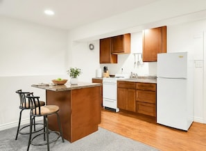 A modern kitchen with wooden cabinets, a white refrigerator, and a central island with bar stools. - 2-bedroom apartment in peaceful Seattle neighborhood near beach and downtown (Seattle)