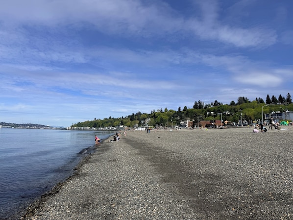 A pebbled beach with people, a calm sea, and a forested hillside in the background. - 2-bedroom apartment in peaceful Seattle neighborhood near beach and downtown (Seattle)
