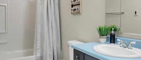A bathroom with a bathtub, toilet, vanity with a sink, and a mirror.