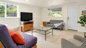 Een woonkamer met een bank, fauteuil, glazen salontafel, televisie en een deur.