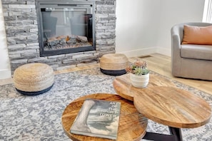 Ein Wohnzimmer mit Kamin aus Stein, einem runden Couchtisch aus Holz und einem grauen Sofa.