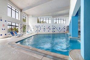 Ein Innenpool mit klarem, blauen Wasser, umgeben von blau-weißen Fliesenwänden und ausgestattet mit Liegestühlen.
