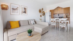 Una sala moderna con un sofá, una mesita de centro, un comedor con sillas y una cocina al fondo.