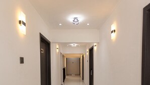 En hotellkorridor med ett glänsande, kaklat golv, mörka dörrar och väggmonterade lampor.