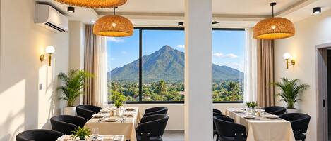 A dining area with tables set for a meal, large windows with a mountain view, and hanging wicker lamps.