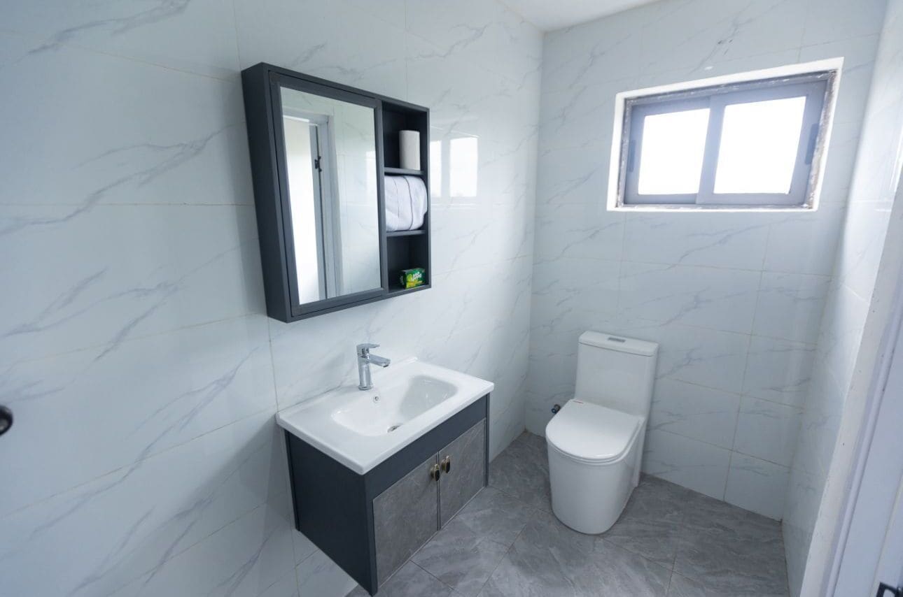 A bathroom with a white sink, dark cabinet, toilet, and a window.