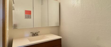 A bathroom with a white sink, a mirror with lights, wooden cabinets, and a toilet.