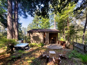 A rustic cabin with a hot tub, surrounded by tall trees and a wooden deck. - Sea Pony | Ocean Views, Hot Tub, Family Friendly (Sea Ranch)