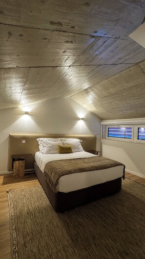 Un dormitorio con cama, mesitas de noche, una alfombra y techo inclinado.