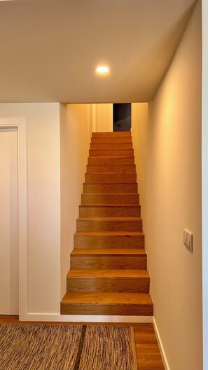 Una escalera de madera en un pasillo con suelo alfombrado y una puerta a la izquierda.