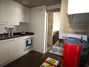 A compact kitchen with white cabinets, a stove, and a red trash bin. - APARTAMENTO VORAMAR by Interhome (Alicante)