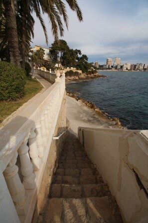 A coastal walkway with a stone staircase leading to a beach, palm trees, and a cityscape in the background. - APARTAMENTO VORAMAR by Interhome (Alicante)