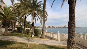 A coastal promenade with palm trees, a white balustrade, and a view of a city skyline across the water. - APARTAMENTO VORAMAR by Interhome (Alicante)