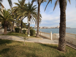 Eine Uferpromenade mit Palmen, einer weißen Balustrade und Blick auf einen Stadt-Horizont über dem Wasser.