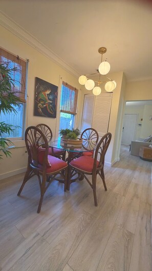 A dining area with a glass table, wooden chairs, a hanging light fixture, and a painting on the wall. - Suarez Art Stay, Coconut Grove, 2 free parking (Miami)