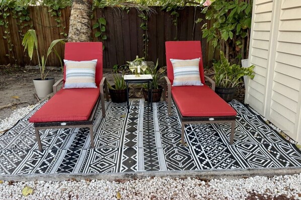 Two red lounge chairs with patterned cushions, a small table with a bottle and glass, and a decorative rug on a gravel surface. - Suarez Art Stay, Coconut Grove, Sleeps 5, Park (Miami)