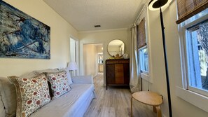 Una habitación con un sofá, un armario de madera, un espejo redondo y una ventana con persianas.