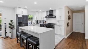 Cocina moderna con armarios blancos, una isla central con taburetes, estufa y campana extractora negra.