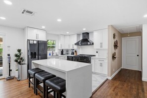 Une cuisine moderne avec des meubles blancs, un îlot central doté de tabourets, une cuisinière et une hotte noire.