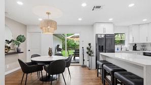 Una cocina moderna con armarios blancos, una isla central y un comedor con una mesa redonda y sillas.