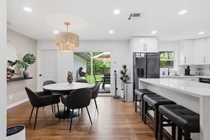 A modern kitchen with white cabinetry, a central island, and a dining area with a round table and chairs. - Upscale 4 Bd/3 Ba 5 Min to the Galleria! (Houston)