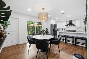 Une cuisine moderne avec des meubles blancs, un réfrigérateur noir et un coin repas comprenant une table ronde et des chaises noires.