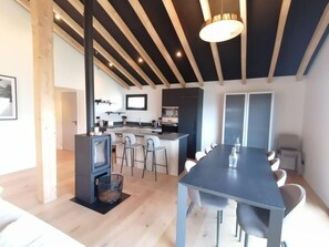 A modern kitchen with a central island, a dining area with a long table, and a built-in wood-burning stove. - Chalet, Ground floor, terrace, fireplace or stove, tv, 151m², Montalbert (Aime)